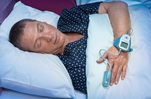 Man sleeping with at home sleep apnea testing device