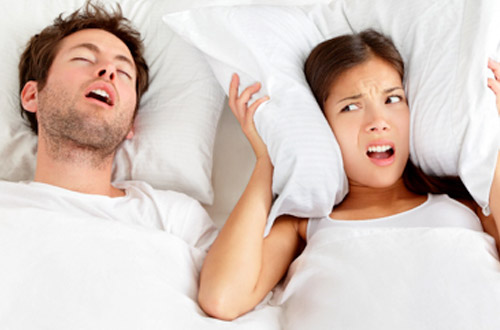 Woman covering ears next to snoring man