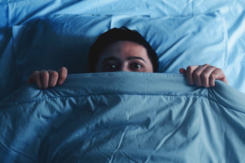 A scared man holding his bed sheets in front of his face