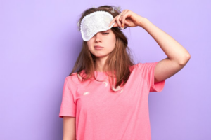 Woman groggily lifting a sleep mask off her face