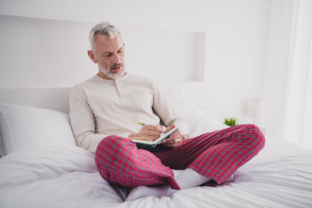 A man in bed writing in a sleep diary